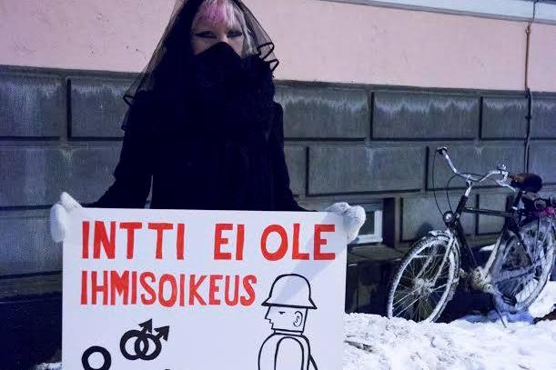 Tummiin pukeutunut henkilö seisoo lumisella kadulla pitäen kylttiä: Intti ei ole ihmisoikeus. Elämä on.